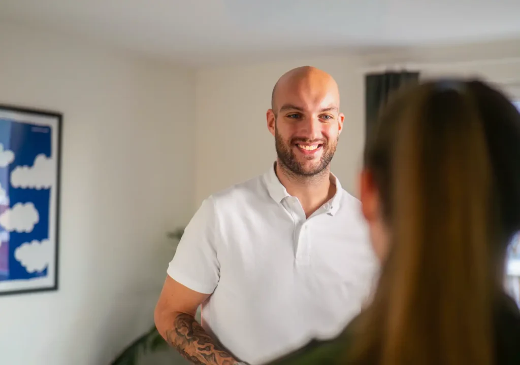 Un homme chauve et barbu de 30 ans, souriant, en polo blanc. Il a des tatouages sur les bras. C'est Walther Herman, le directeur d'hreimmo. Il regarde un client que l'on voit de dos lors d'un rendez-vous.
